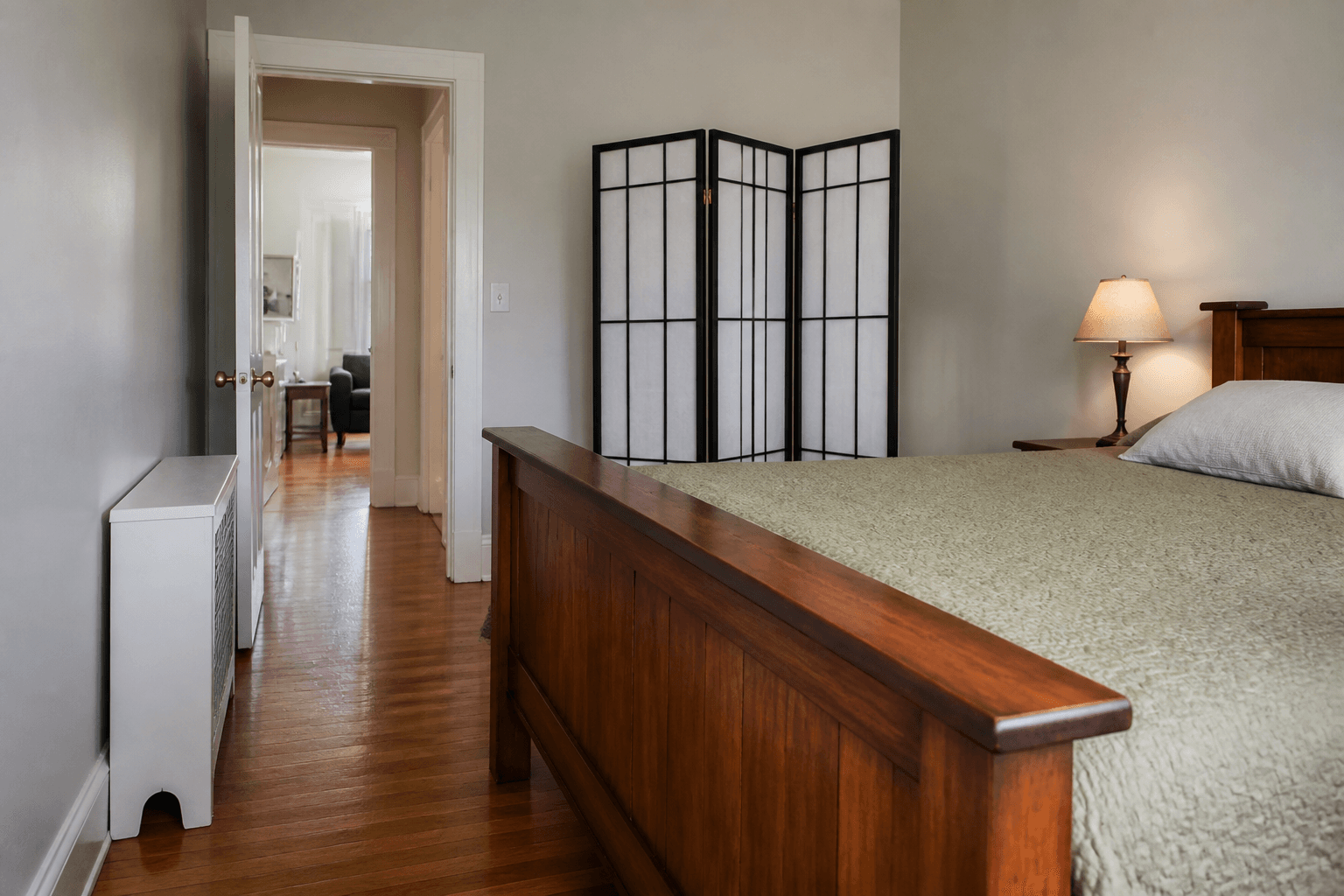 Wood footboard on a bed still aimed at an open door, folding screen beside the walk