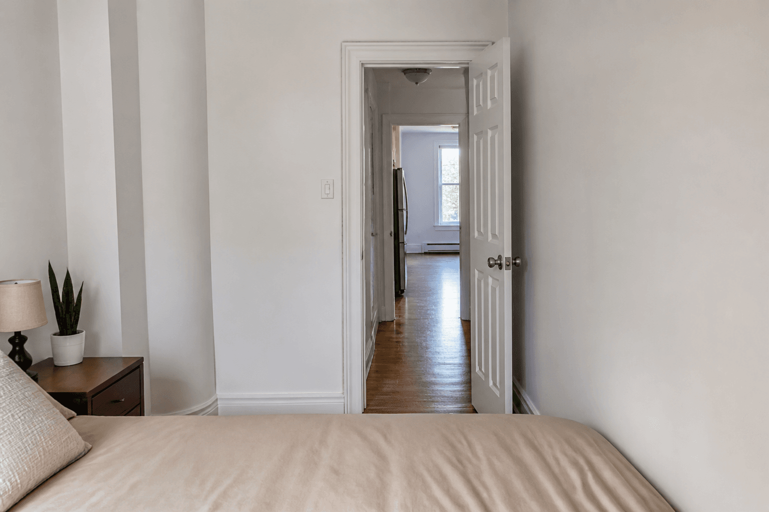 Beige bed aimed straight at an open bedroom door on a wood floor path, feng shui bed facing door