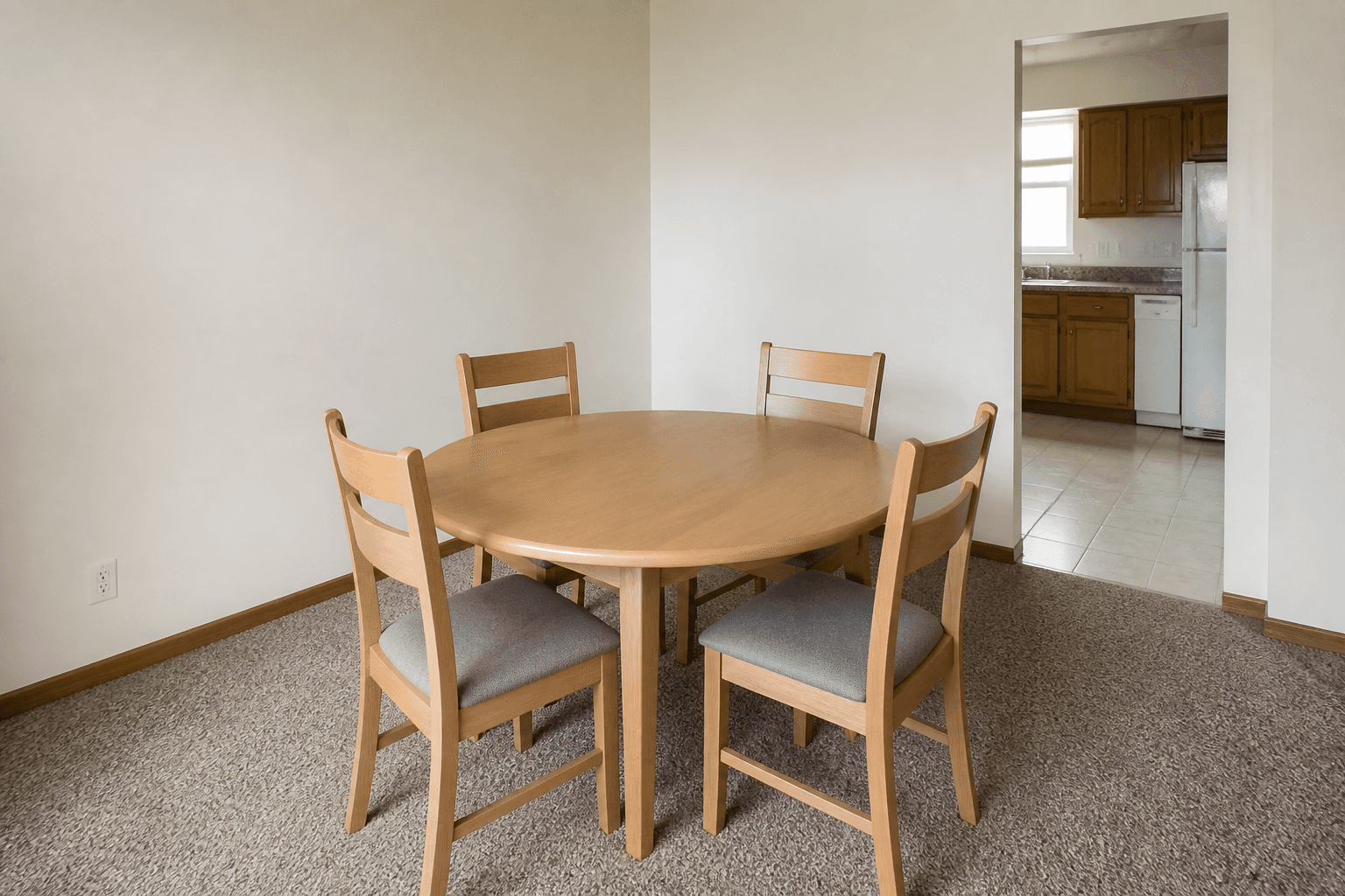 Round light-oak dining table with four ladder-back chairs, cream walls, kitchen doorway beyond, feng shui dining table shape