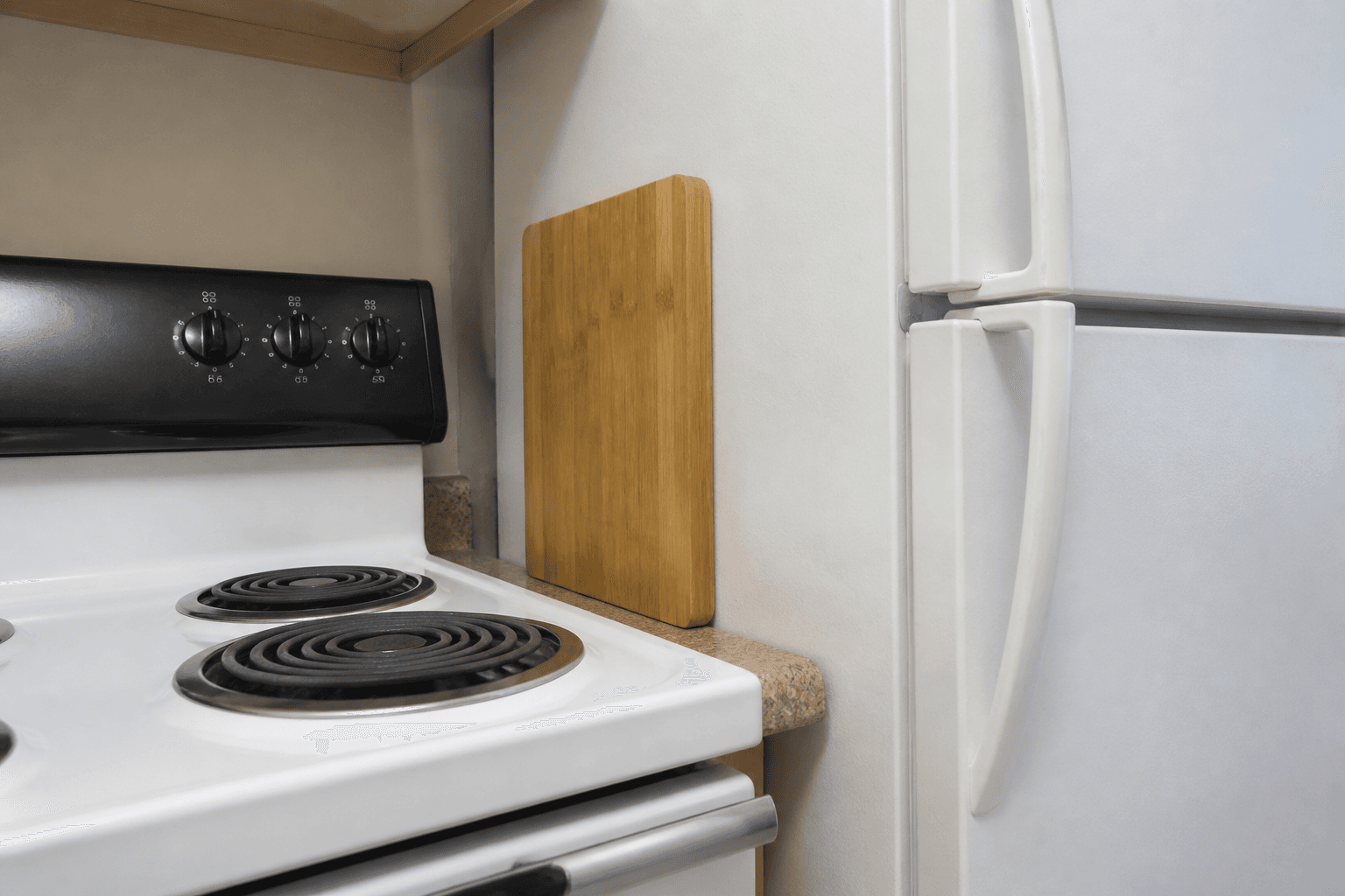 White fridge beside a stove with a standing wood board as a buffer on the counter