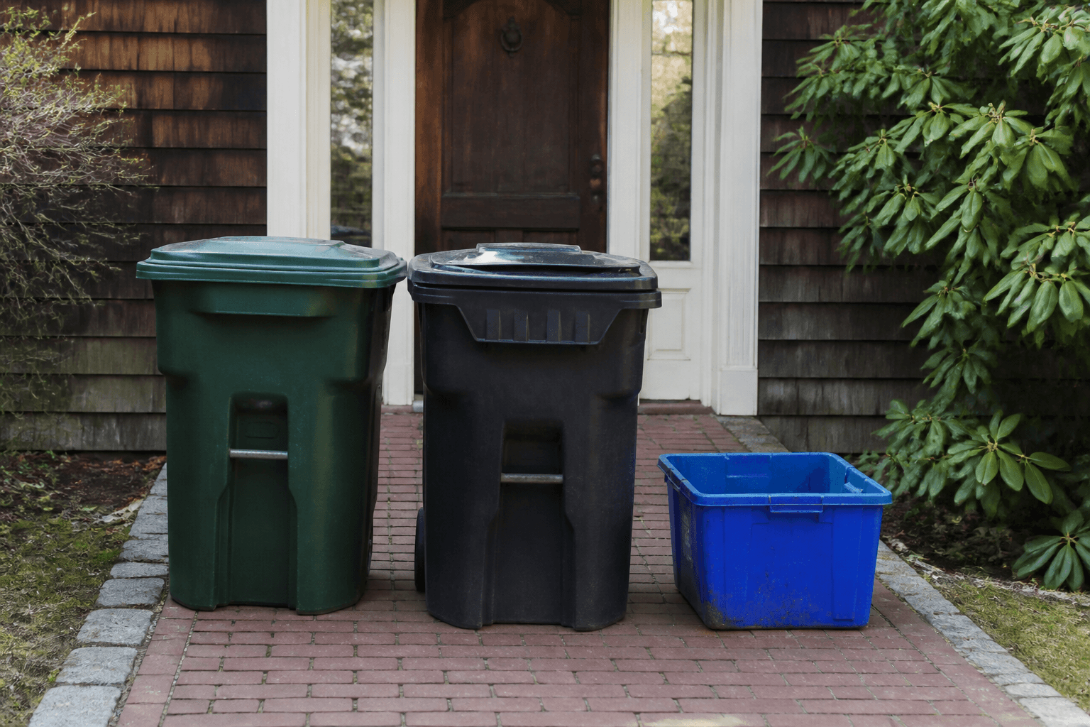 Trash bins and a crate parked on a brick path, blocking the walk to the house