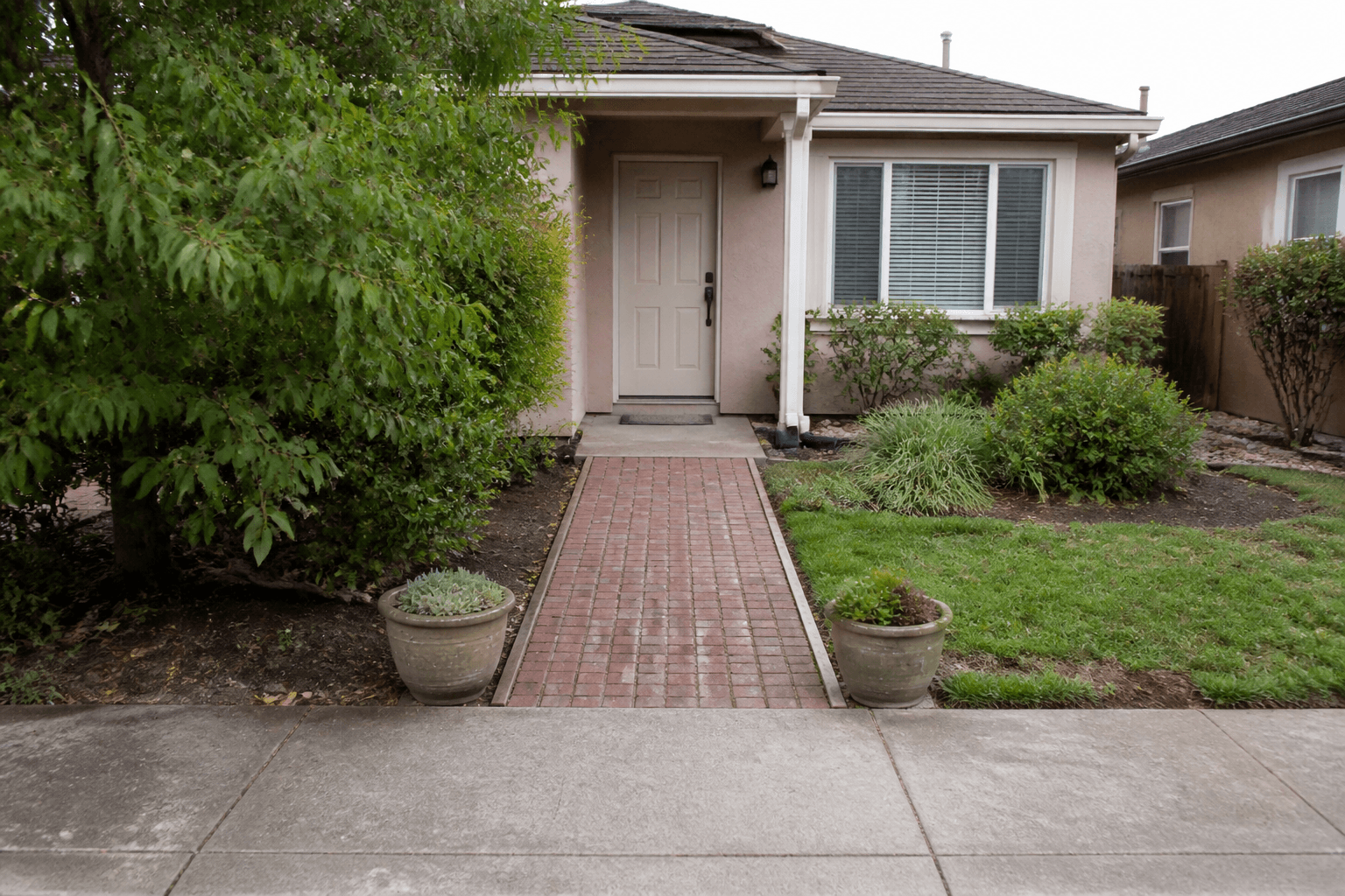 Brick front path from the sidewalk to a beige house door, pots beside the walk, feng shui front yard path