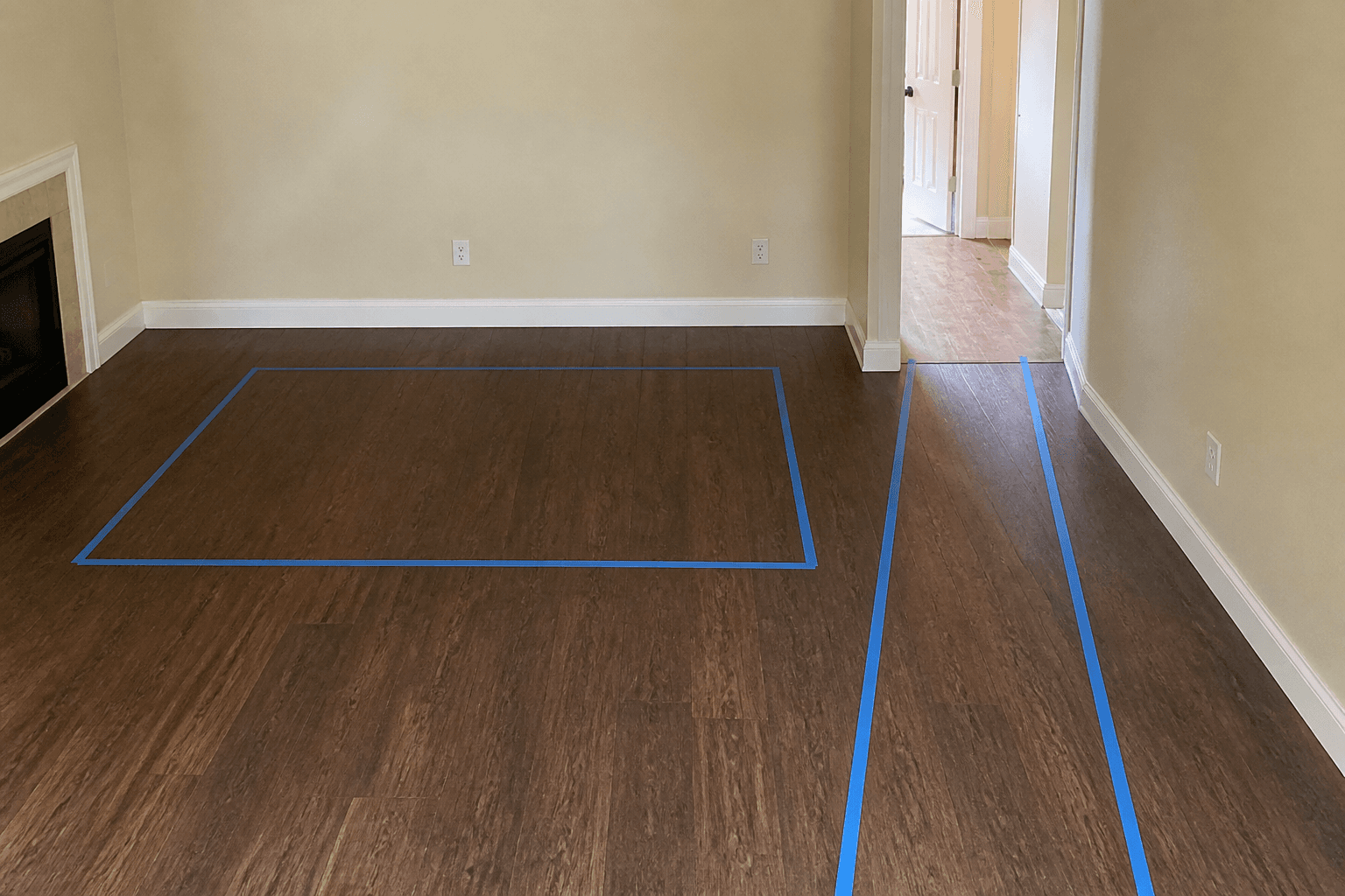 Blue painter tape on a wood floor: a large rectangle and a narrow walk to a doorway