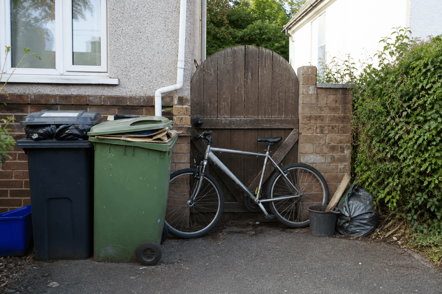 Wooden gate blocked by bins and a bicycle so the leaf cannot swing