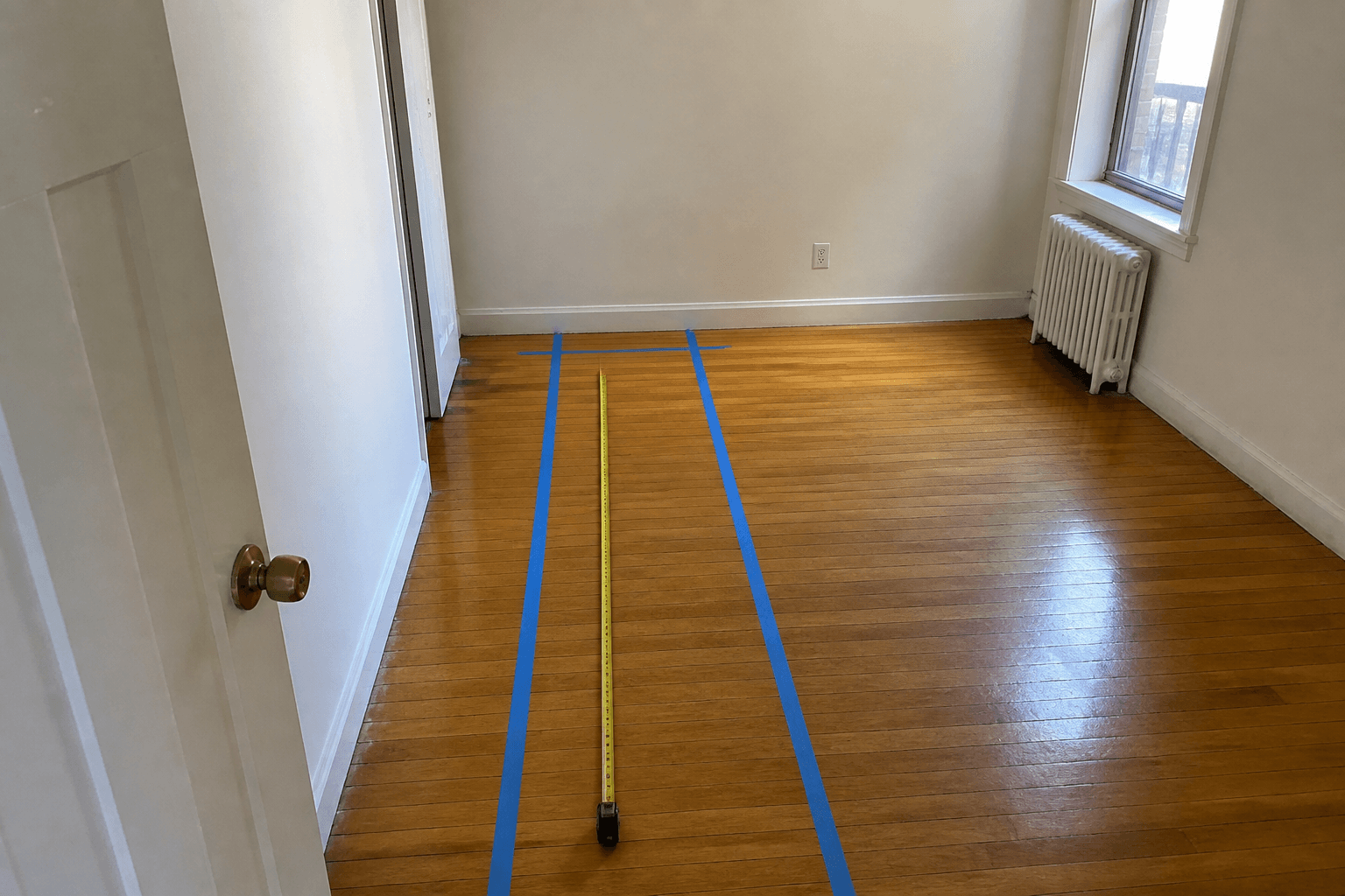 Person walking a taped aisle from a door toward a bed wall, tape measure along the path