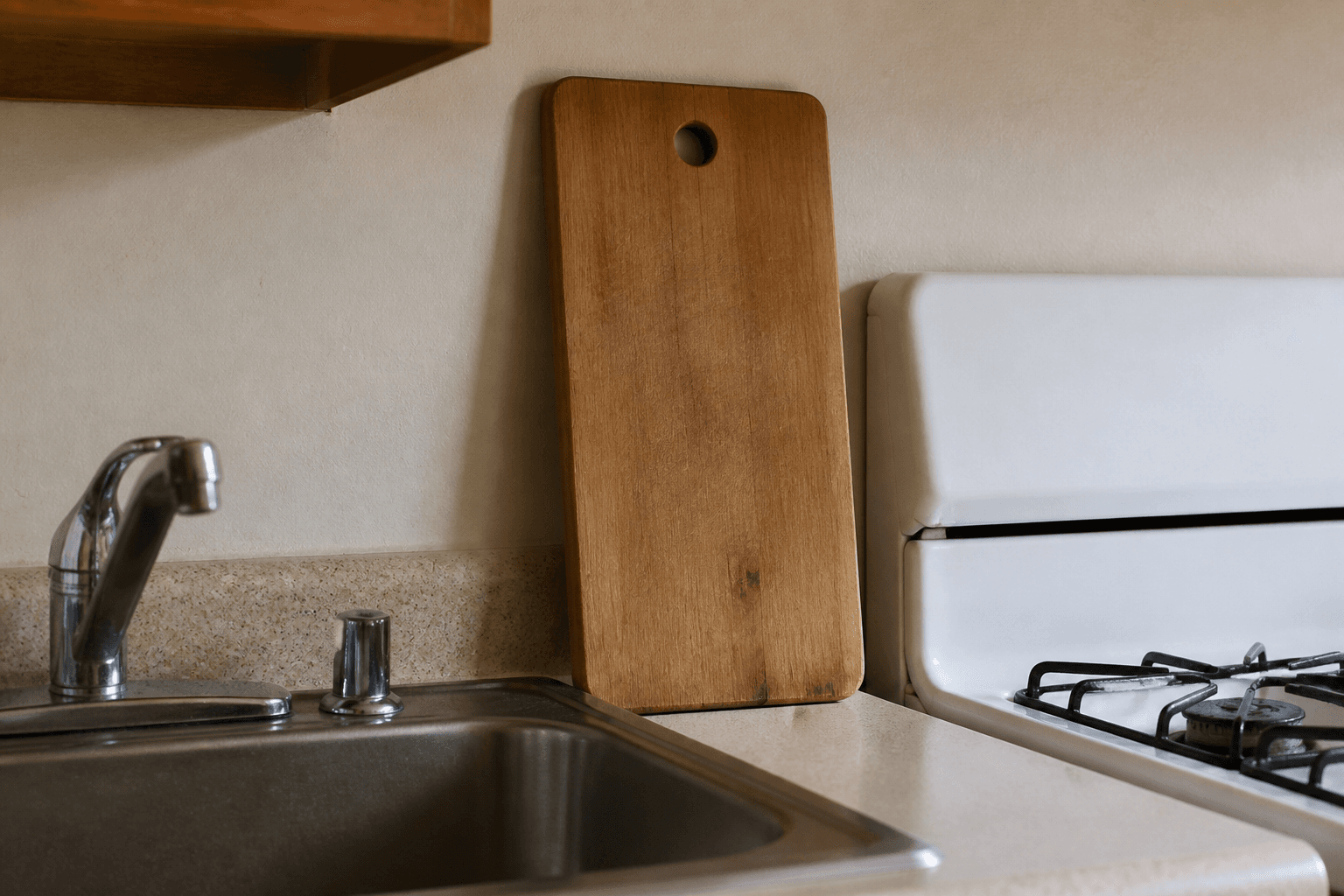 Wood cutting board standing between a stainless sink and a white gas stove