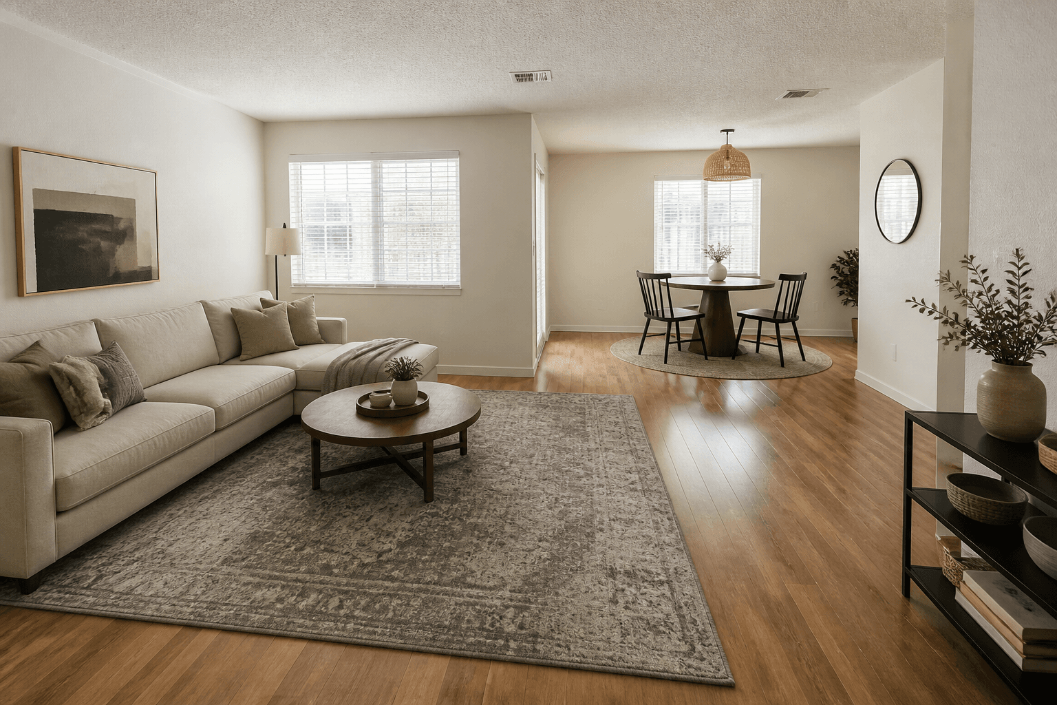 Open L-shaped rental with a living rug and sofa on one leg and a round dining table on a smaller rug, feng shui L-shaped apartment