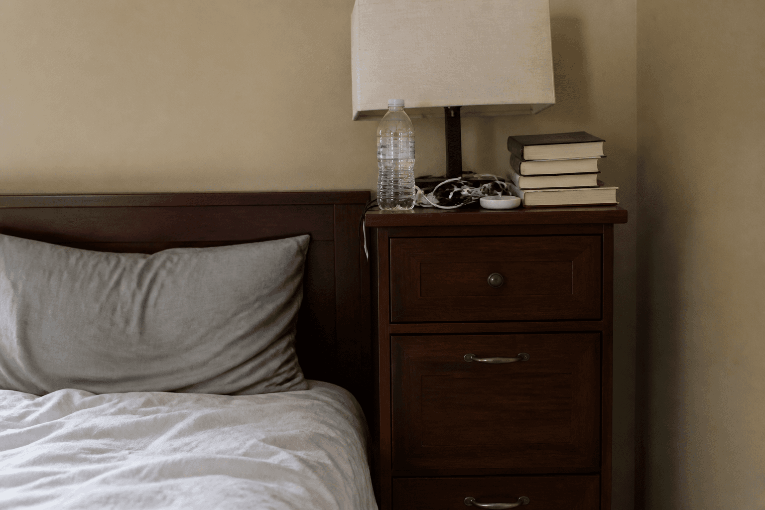 Tall nightstand stacked with a water bottle, books, a small speaker, and charger cords