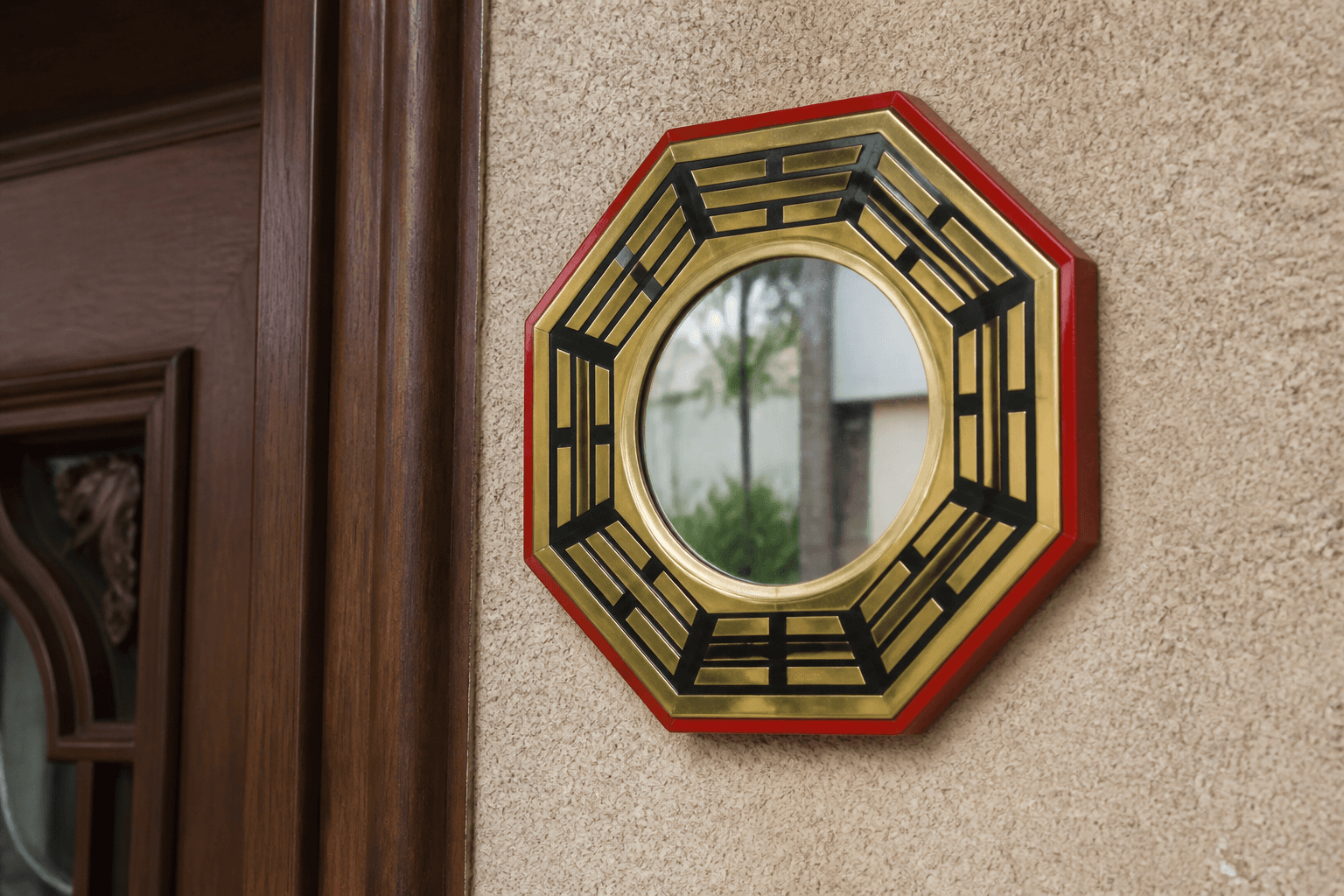 Close view of an octagonal bagua mirror on beige stucco beside a wood door