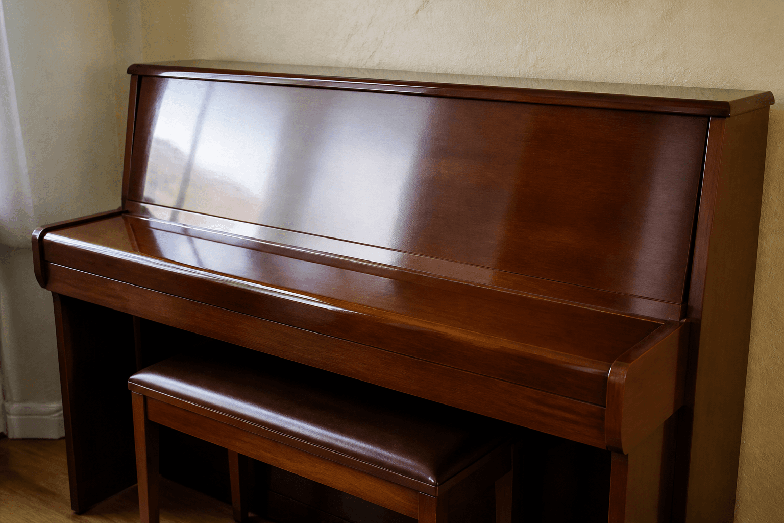 Closed piano lid on an upright against plaster, bench tucked under