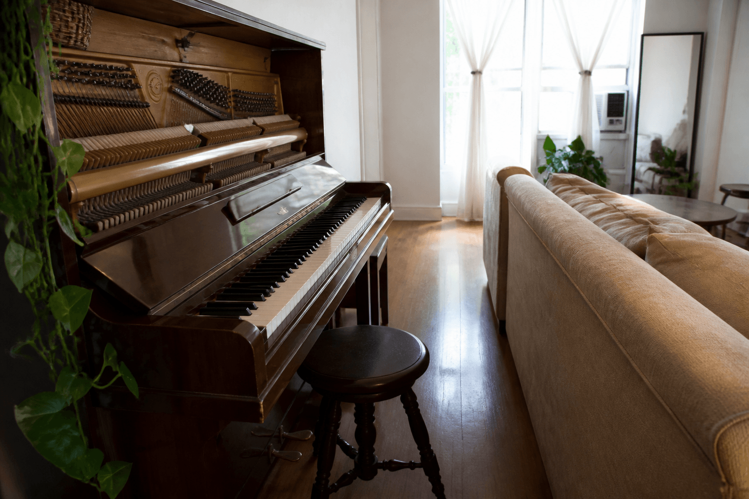Upright piano lid open pinching the walk between the piano and a beige sofa