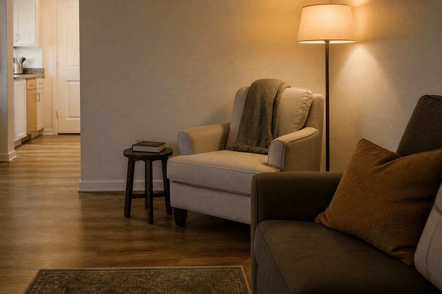 Armchair with its back to a plaster wall, warm floor lamp on, book on a side table, feng shui reading nook