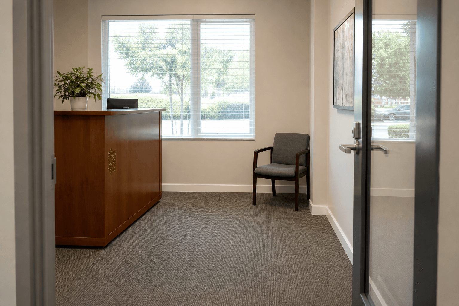 Wood desk to the left of glass doors, clear walk, one waiting chair on a side wall
