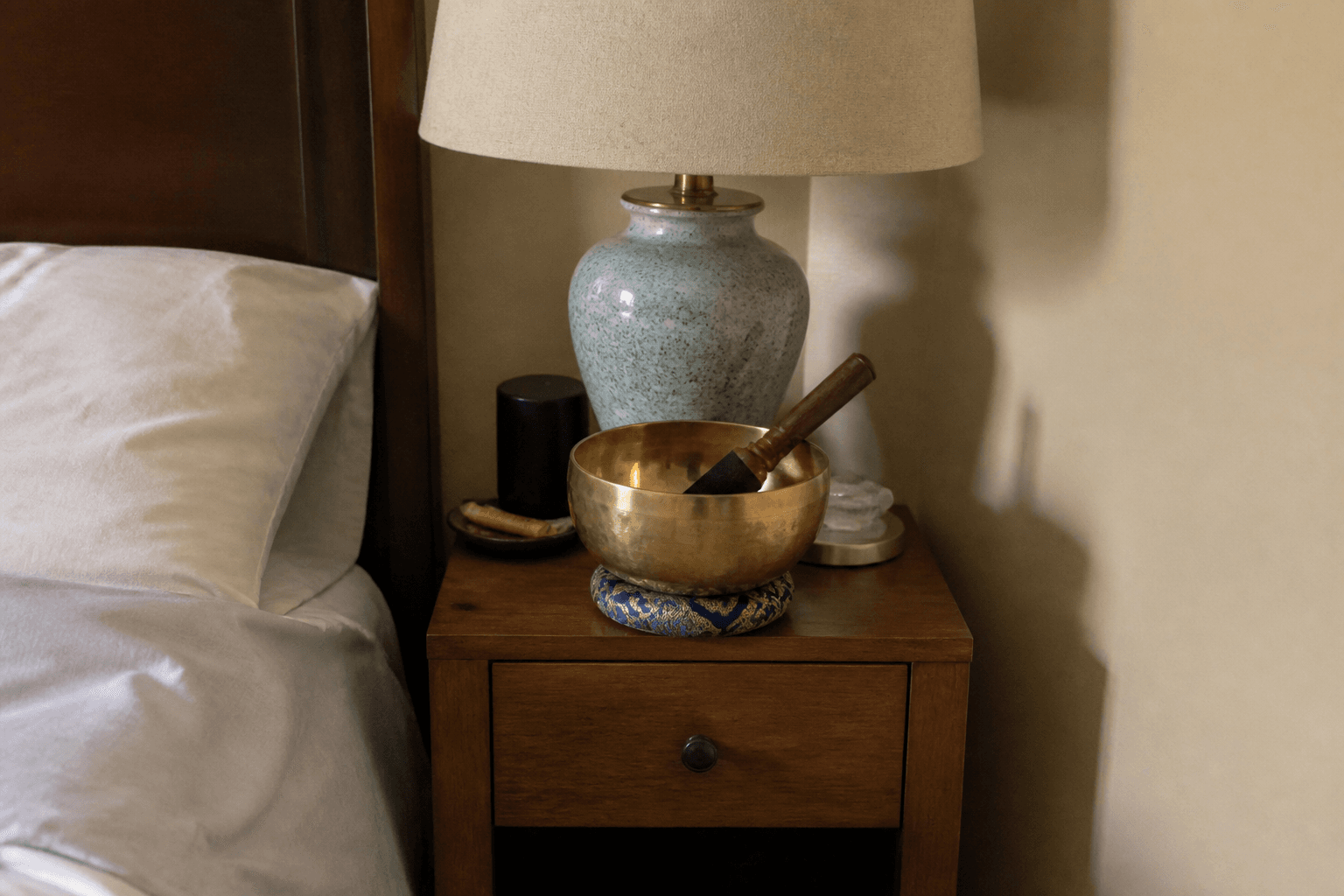 Crowded bedroom nightstand with a lamp and a singing bowl on top