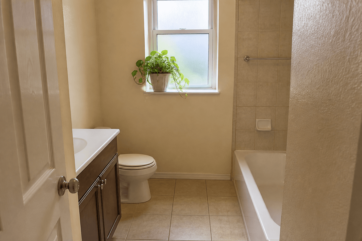 Leafy pot on a bathroom sill, toilet lid closed, beige tile, feng shui bathroom plants