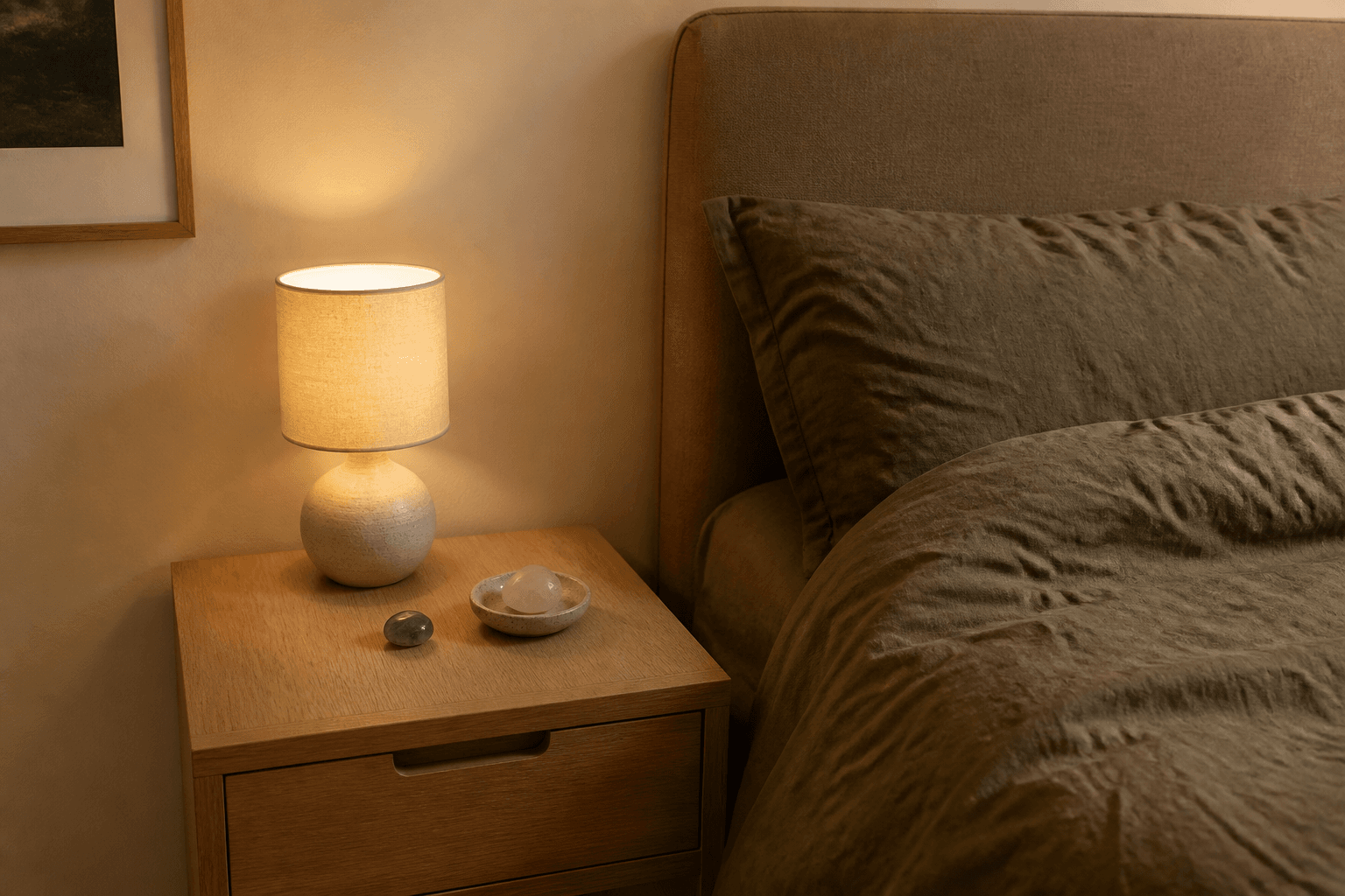 Oak nightstand with a small dish of tumbled stones beside a lamp and fabric headboard, feng shui crystals in the bedroom