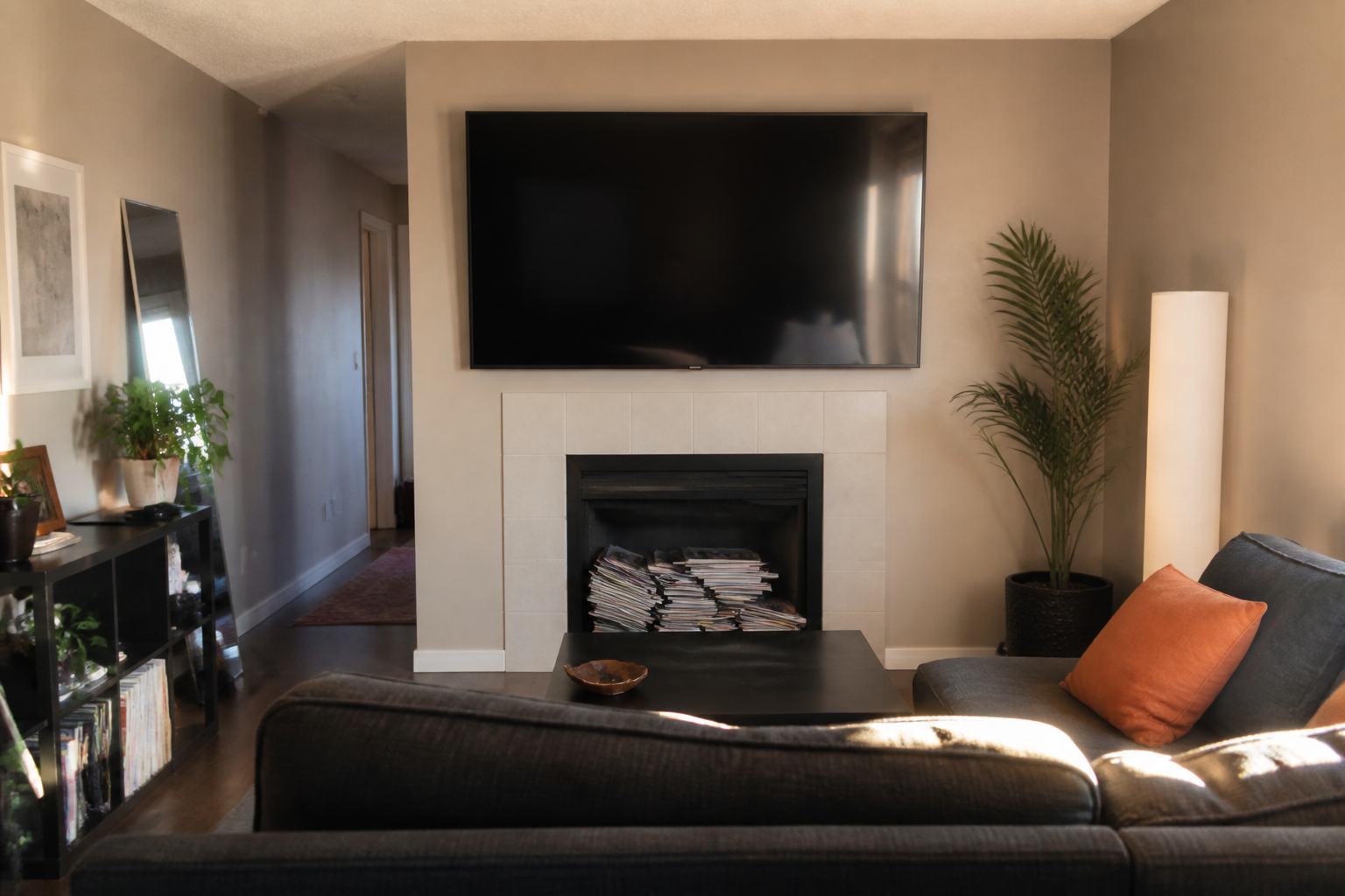 Television mounted over a fireplace with afternoon glare and magazines stuffed in the unused hearth