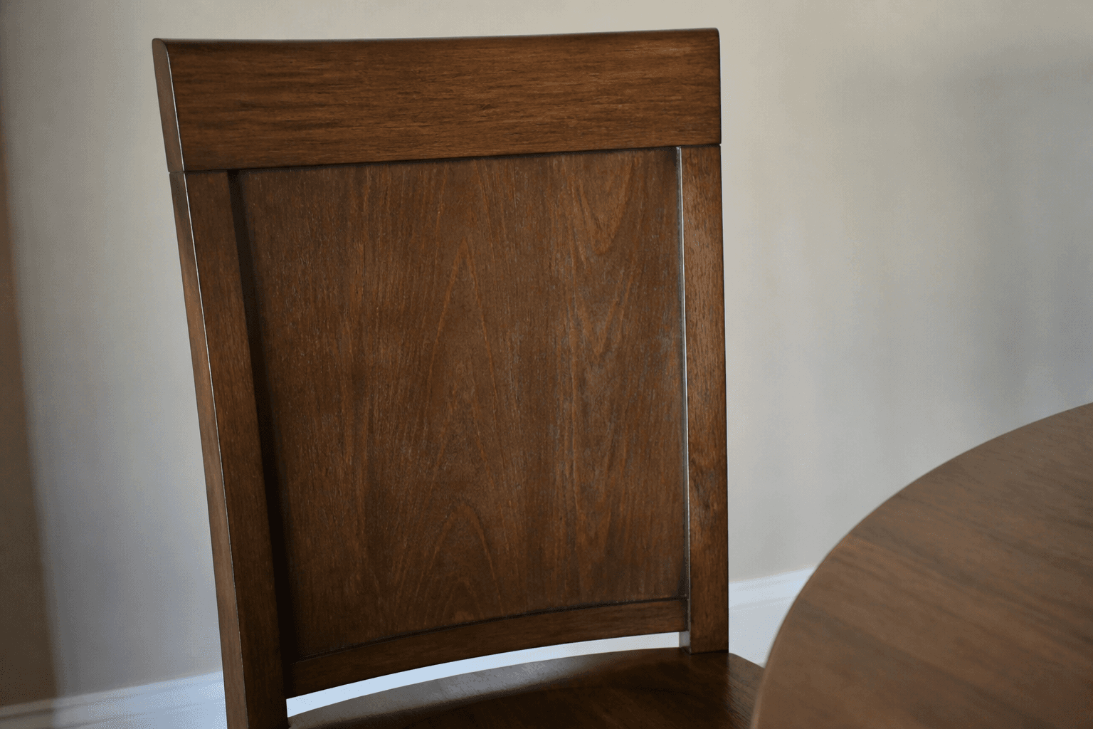 Solid wood dining chair with a closed back against a wall