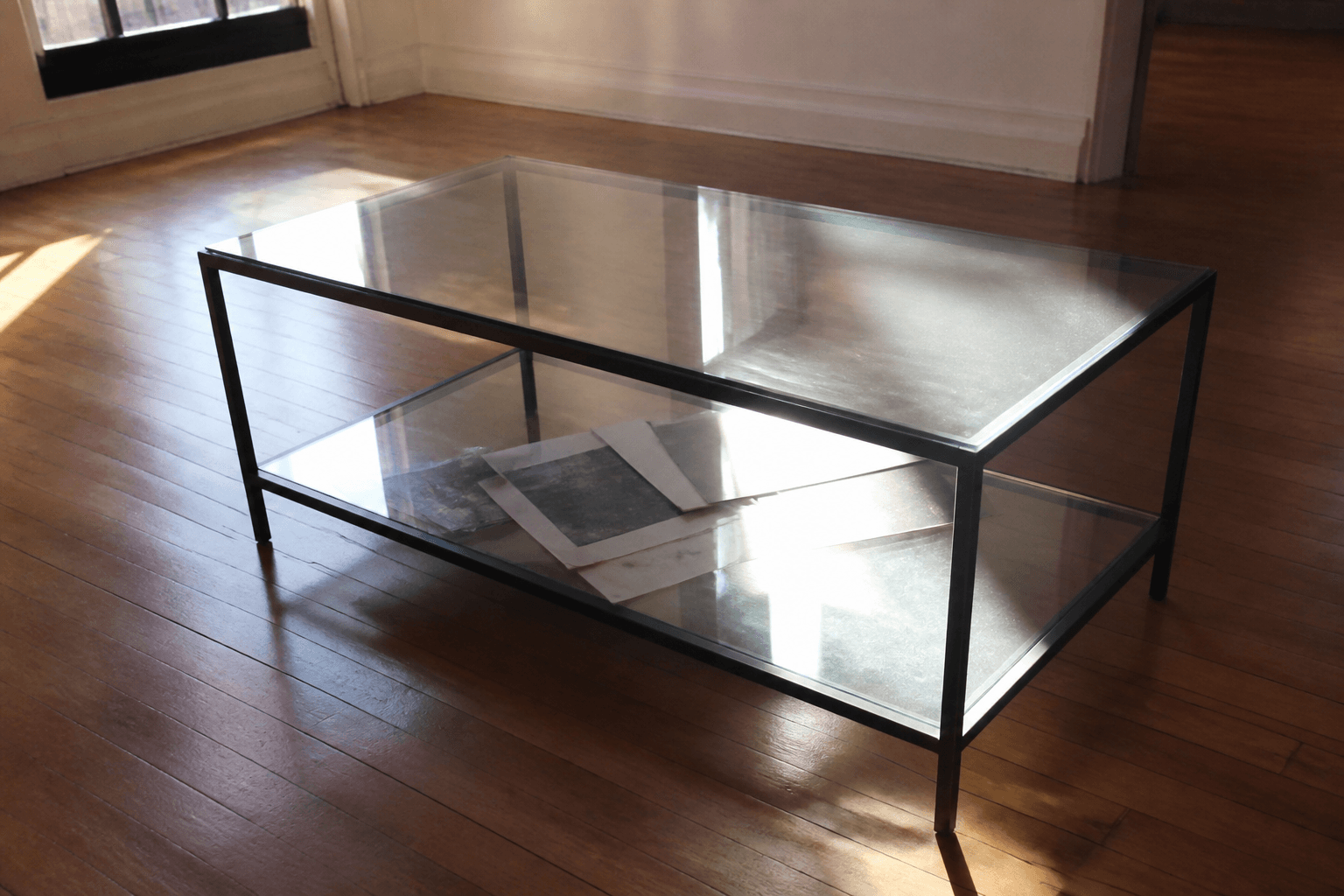 Glass coffee table throwing window glare, papers visible through the top