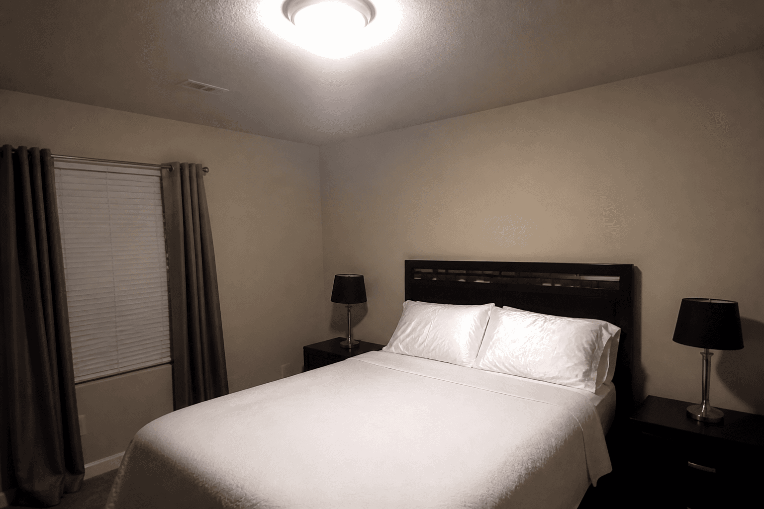 Rental bedroom at night with only a harsh overhead on and dark unused nightstand lamps