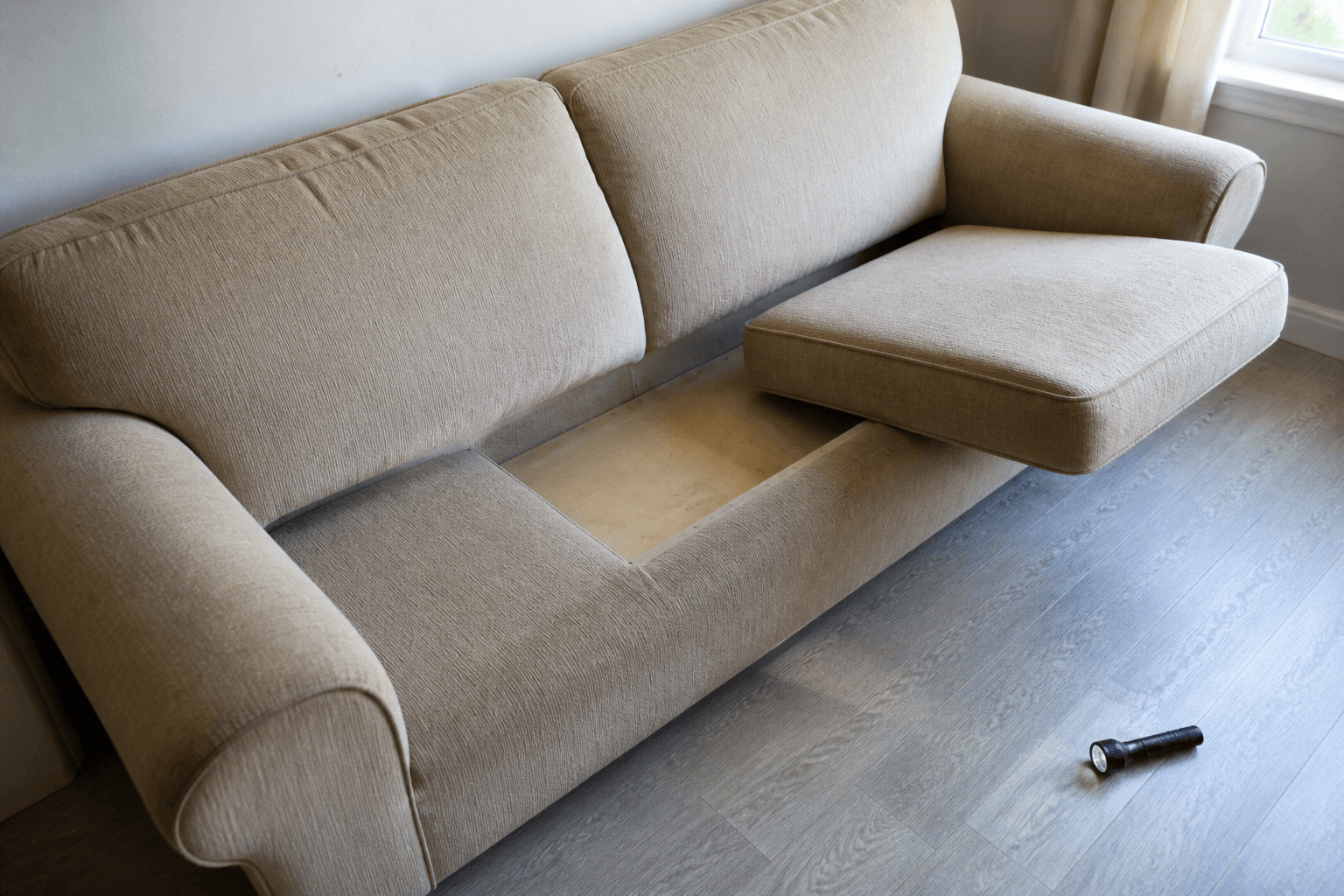 Beige used sofa with one cushion lifted and a flashlight on the floor, feng shui secondhand sofa