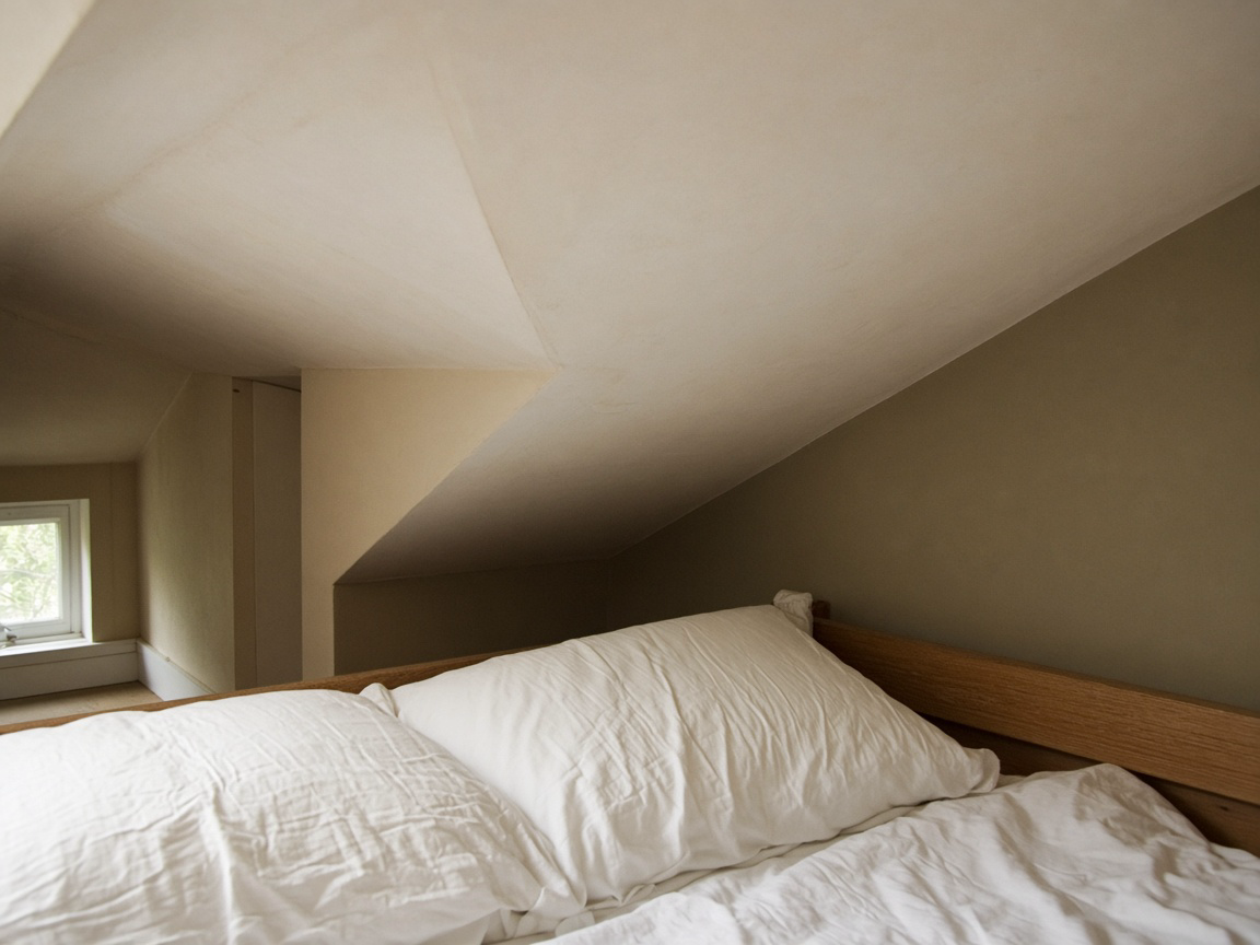 White pillows on a wood bed under a low cream sloped ceiling, looking up from the mattress