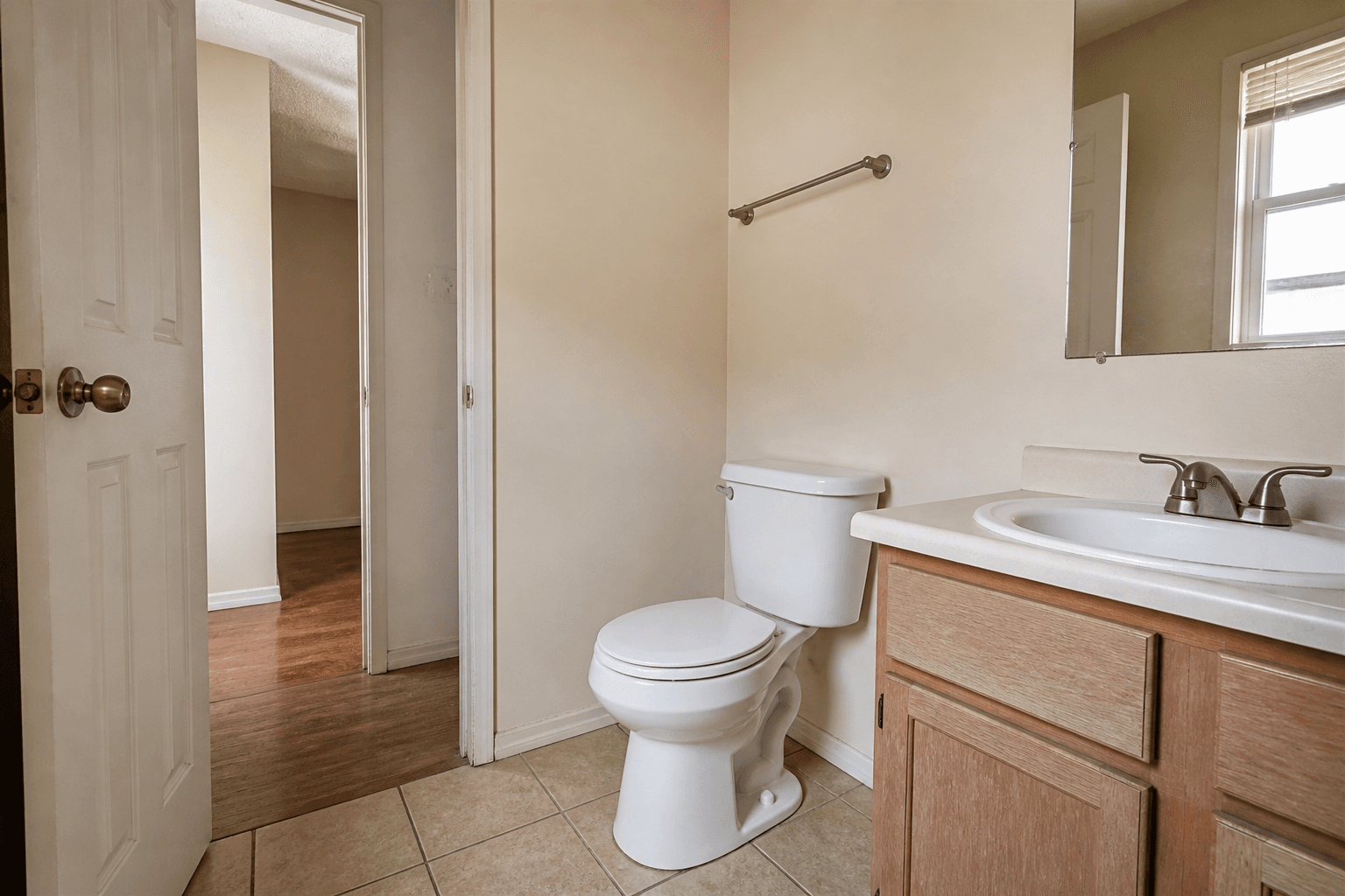 Small beige rental bathroom, white toilet lid closed, door and vanity in daylight, Feng Shui toilet wealth leak
