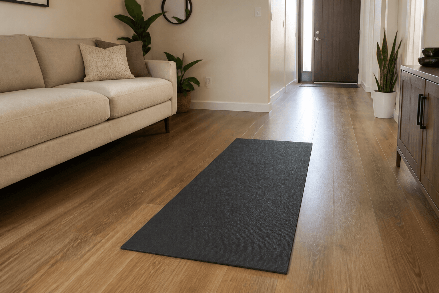 Charcoal yoga mat unrolled on a wood floor with a beige sofa along the wall