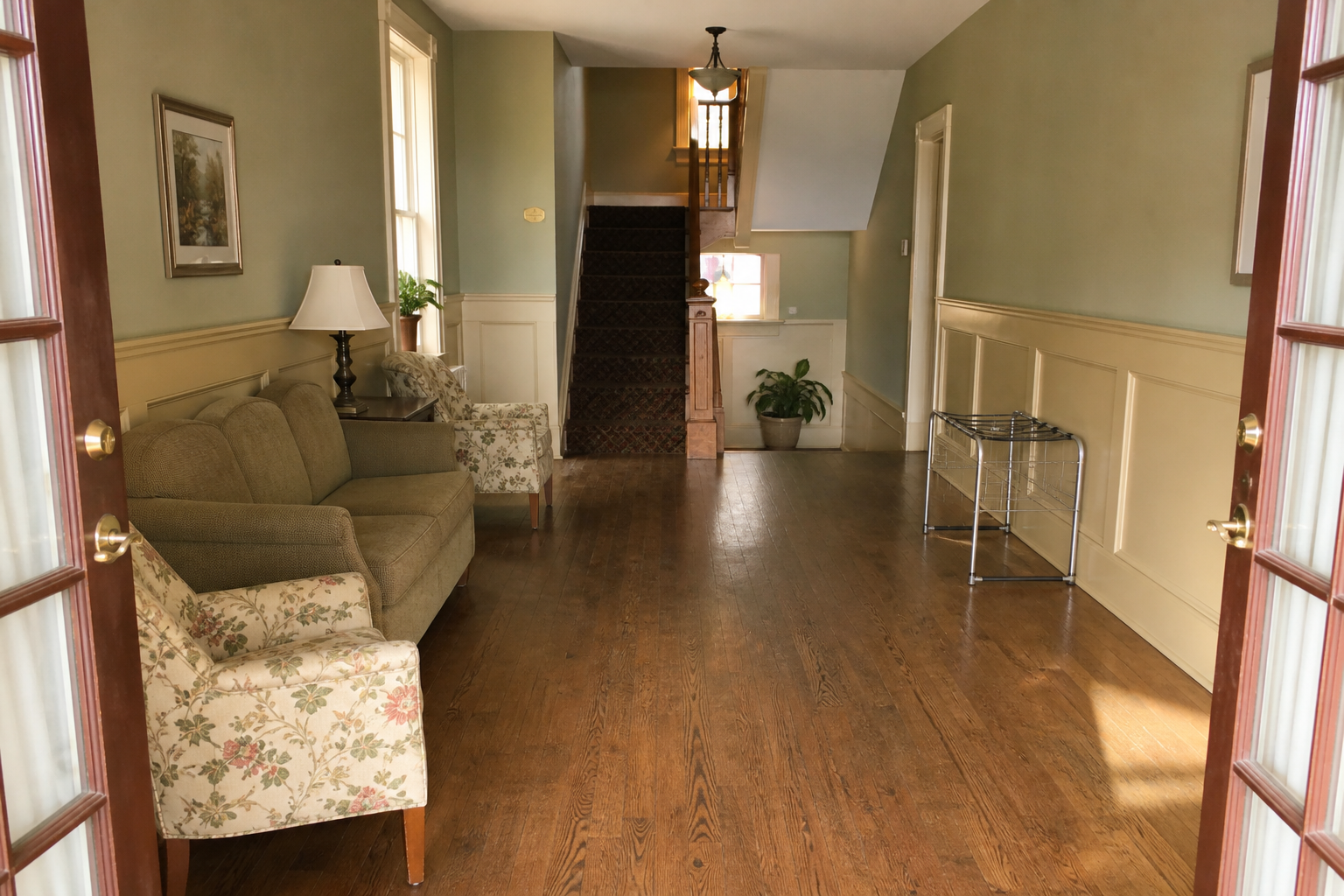 Open inn doors looking toward a carpeted stair, sofa and chairs along the left wall, metal luggage rack on the right