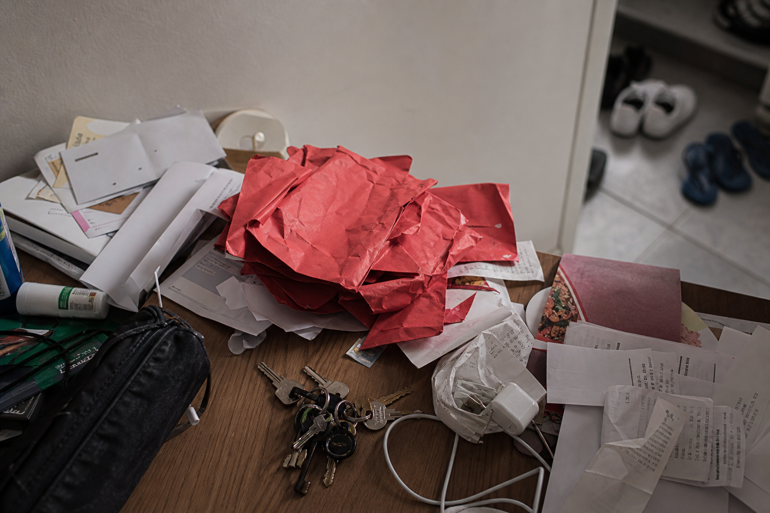 Cluttered entry table with mail, keys, and a crumpled stack of red envelopes dumped among junk