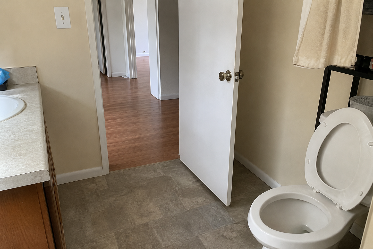 Rental bathroom toilet with the lid up and the door standing open to a hallway