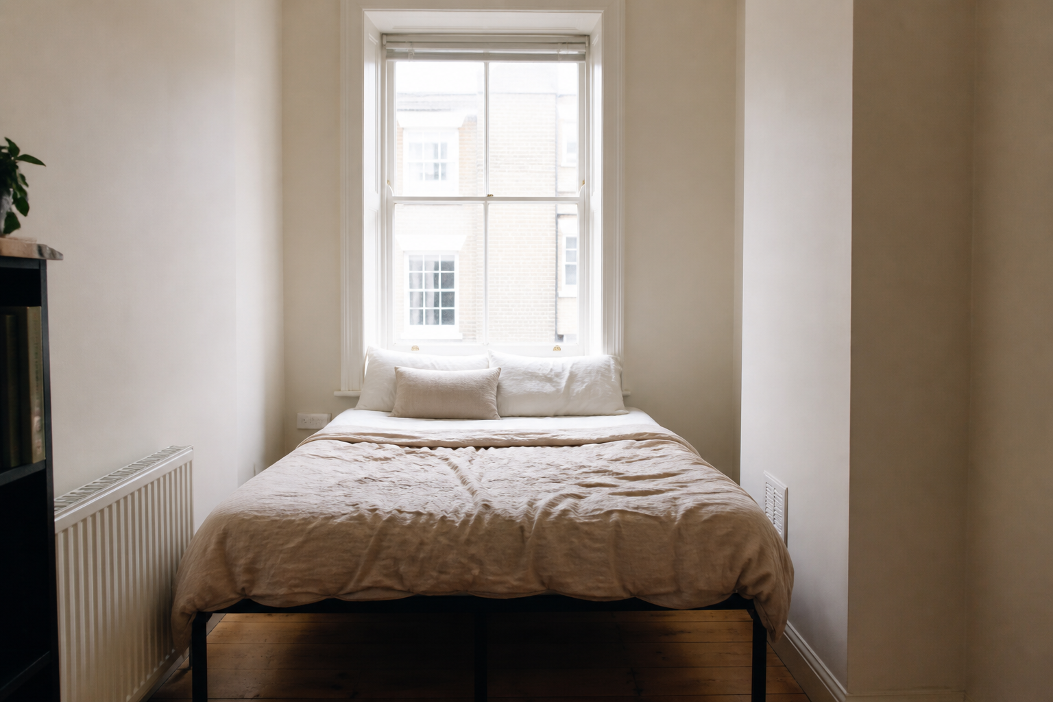 Metal bed with no headboard pushed against a bright window as the only backing