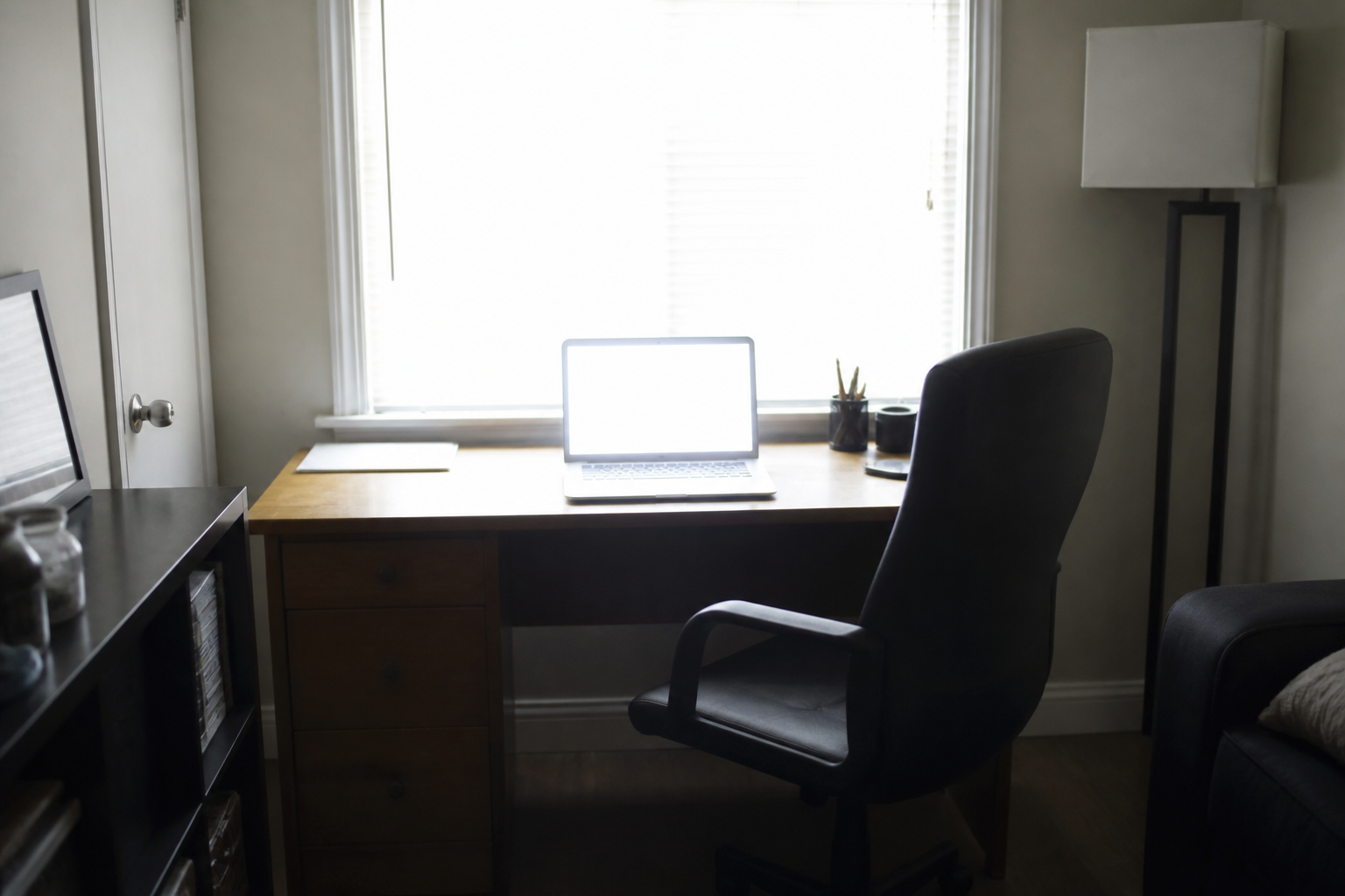 Desk facing a bright window with harsh glare on a laptop screen and an empty chair